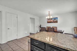 Kitchen with a notable chandelier, light tile patterned flooring, light stone countertops, and decorative light fixtures