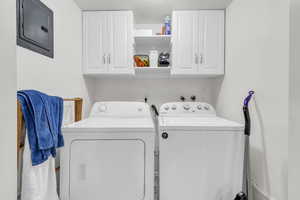 Clothes washing area with cabinets, electric panel, a textured ceiling, and washing machine and dryer