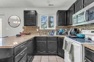 Kitchen featuring black dishwasher, light tile patterned flooring, sink, electric stove, and decorative backsplash