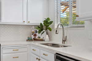 Kitchen with white cabinetry, decorative backsplash, sink, and dishwasher