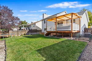 Back of property with a wooden deck, a yard, and a trampoline