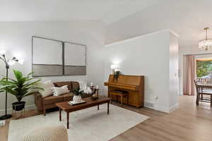 Living room featuring lofted ceiling, an inviting chandelier, and light hardwood / wood-style floors