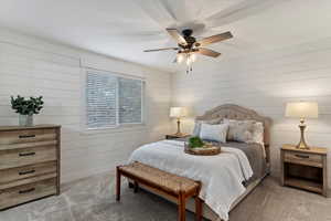 Carpeted bedroom featuring wood walls and ceiling fan