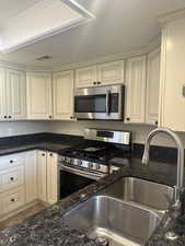 Kitchen with dark stone counters, sink, ornamental molding, appliances with stainless steel finishes, and cream cabinetry