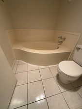 Primary Bathroom with toilet, a washtub, and tile patterned flooring