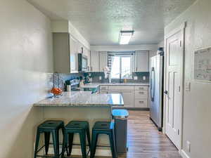 Kitchen with light hardwood / wood-style floors, kitchen peninsula, appliances with stainless steel finishes, tasteful backsplash, and a kitchen bar