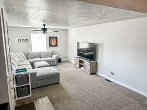 Carpeted living room with a textured ceiling and ceiling fan