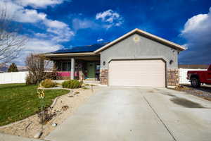 Single story home featuring solar panels, a porch, a garage, and a front yard