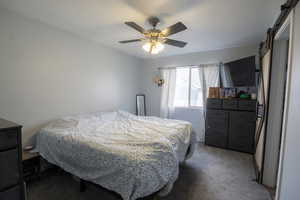 Bedroom with a barn door, ceiling fan, and dark colored carpet