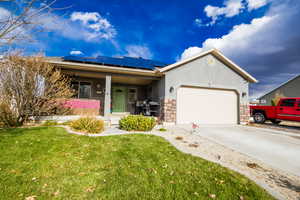 Single story home with a front yard, covered porch, a garage, and solar panels