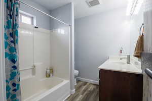 Full bathroom with shower / bathtub combination with curtain, vanity, toilet, and wood-type flooring