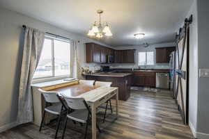 Kitchen with appliances with stainless steel finishes, dark hardwood / wood-style flooring, dark brown cabinets, a barn door, and hanging light fixtures