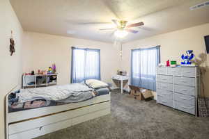 Carpeted bedroom featuring ceiling fan and a textured ceiling