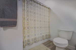 Bathroom with hardwood / wood-style flooring, toilet, and shower / bath combo with shower curtain