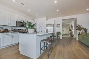 Kitchen with stainless steel appliances, light hardwood / wood-style floors, white cabinetry, and a kitchen island with sink