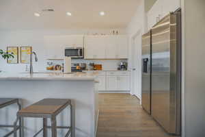 Kitchen featuring white cabinets, a kitchen bar, stainless steel appliances, and light wood-type flooring