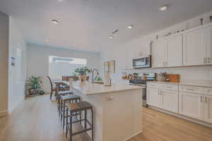 Kitchen featuring white cabinets, appliances with stainless steel finishes, light hardwood / wood-style floors, and an island with sink