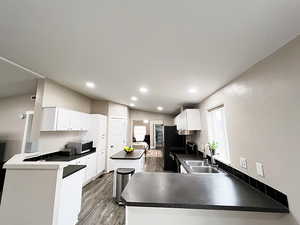 Kitchen featuring vaulted ceiling, electric stove, kitchen peninsula, sink, and white cabinetry