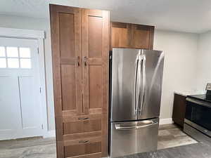 Kitchen featuring a textured ceiling, stainless steel appliances, light hardwood / wood-style floors, and stone countertops