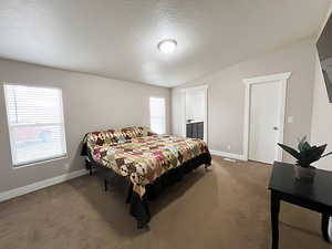 Bedroom featuring ensuite bath, a textured ceiling, lofted ceiling, and dark carpet