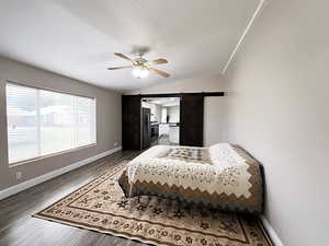 Bedroom with a barn door, ceiling fan, dark hardwood / wood-style floors, and lofted ceiling