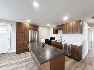 Kitchen featuring sink, appliances with stainless steel finishes, a textured ceiling, light hardwood / wood-style flooring, and a center island