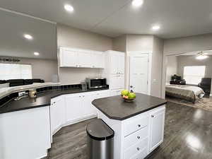 Kitchen with dark wood-type flooring, a kitchen island, ceiling fan, and white cabinets