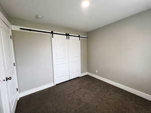 Unfurnished bedroom with a closet, a barn door, and dark colored carpet