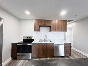 Kitchen featuring appliances with stainless steel finishes, sink, light stone counters, and wood-type flooring