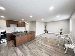 Kitchen with a kitchen island, appliances with stainless steel finishes, dark brown cabinets, sink, and light hardwood / wood-style flooring