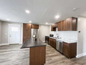 Kitchen with light hardwood / wood-style floors, stainless steel appliances, a center island, a textured ceiling, and sink