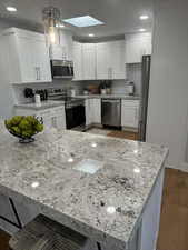 Kitchen featuring stainless steel appliances, white cabinetry, a skylight, hardwood / wood-style floors, and pendant lighting