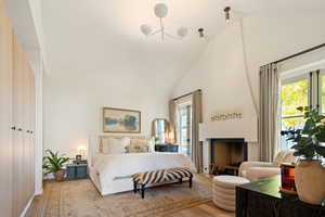 Bedroom with a large fireplace, high vaulted ceiling, and light hardwood / wood-style floors