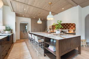 Kitchen with a large island, light stone countertops, decorative light fixtures, and light wood-type flooring