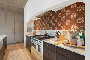 Kitchen with light hardwood / wood-style floors, high end white range, decorative backsplash, and dark brown cabinetry