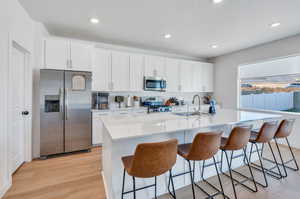 Kitchen with light wood-type flooring, appliances with stainless steel finishes, an island with sink, a breakfast bar, and white cabinets