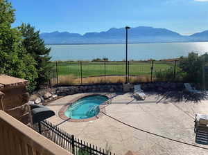 View of swimming pool with a patio, fence, a water and mountain view, and an in ground hot tub