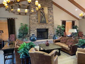 Living area featuring high vaulted ceiling, beam ceiling, a stone fireplace, and an inviting chandelier