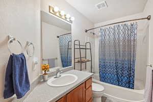 Full bathroom featuring toilet, shower / bath combo, vanity, and a textured ceiling