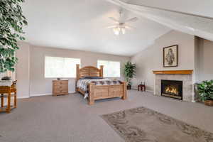 Bedroom featuring a tiled fireplace, lofted ceiling, a textured ceiling, carpet, and ceiling fan