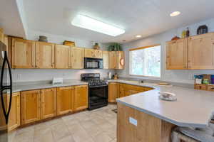 Kitchen featuring black appliances, a textured ceiling, a kitchen bar, sink, and kitchen peninsula