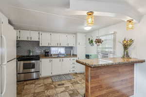 Kitchen featuring white cabinetry, stainless steel range with gas cooktop, decorative backsplash, and white fridge