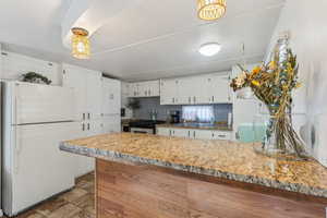 Kitchen featuring backsplash, white refrigerator, pendant lighting, sink, and white cabinets