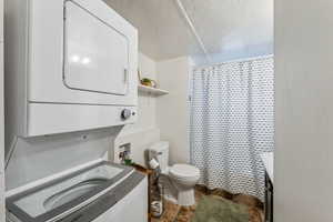 Bathroom with stacked washing maching and dryer, walk in shower, and toilet