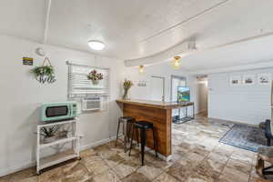 Kitchen with wood walls, a breakfast bar, kitchen peninsula, a textured ceiling, and cooling unit