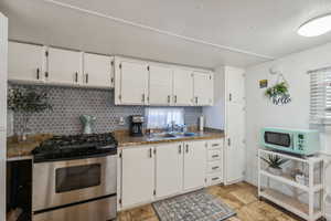 Kitchen with tasteful backsplash, sink, white cabinets, dark stone countertops, and stainless steel range with gas stovetop