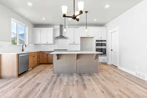 Kitchen with a center island, wall chimney exhaust hood, decorative light fixtures, white cabinetry, and stainless steel appliances