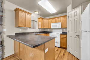 Kitchen with light wood-type flooring, a textured ceiling, white appliances, sink, and kitchen peninsula