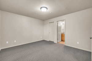 Unfurnished bedroom with a textured ceiling, carpet floors, and ensuite bath