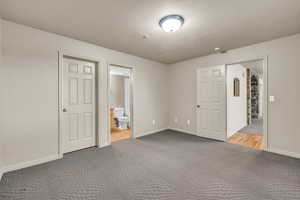 Unfurnished bedroom featuring carpet, ensuite bath, a textured ceiling, and a closet